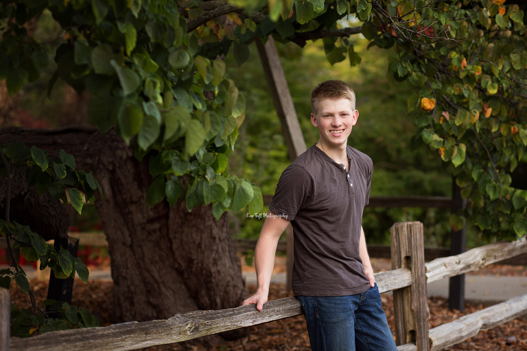 Senior boy leaning up against a wooden fence outside before the sun sets | Portrait Photographer in Midland, Bay City and Saginaw, MI