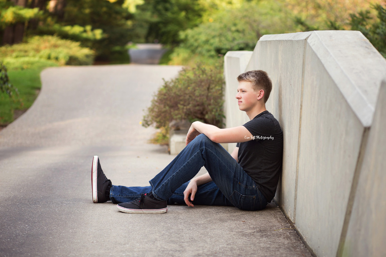 Senior guy sitting down on a concrete bridge with one arm on his leg. Midland, Michigan photographer