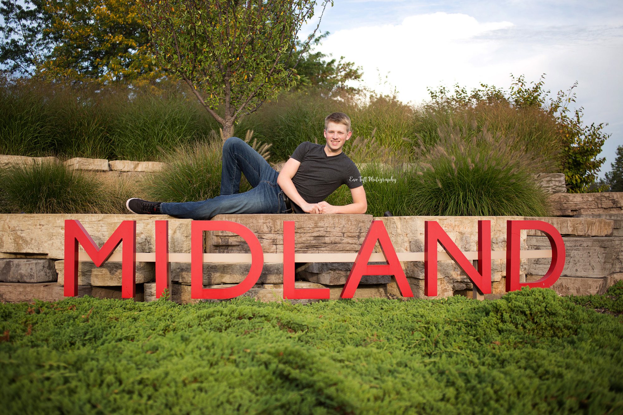 Senior boy laying across a large sign that says Midland. Michigan photographer