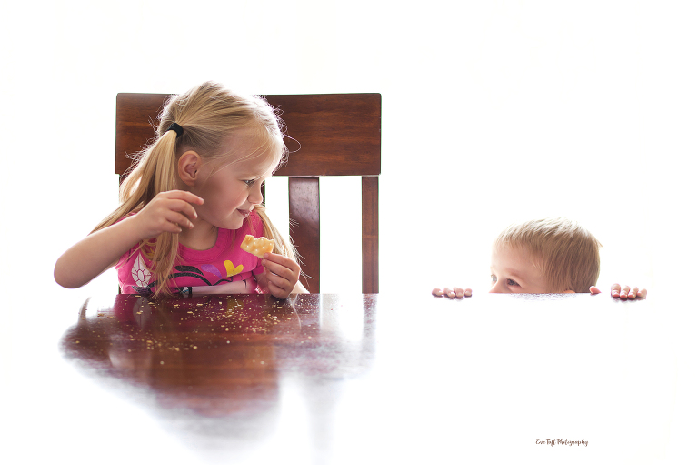 Little girl with pigtails feeding her younger brother a cracker. Professional Photographer in the tri-city area in Michigan