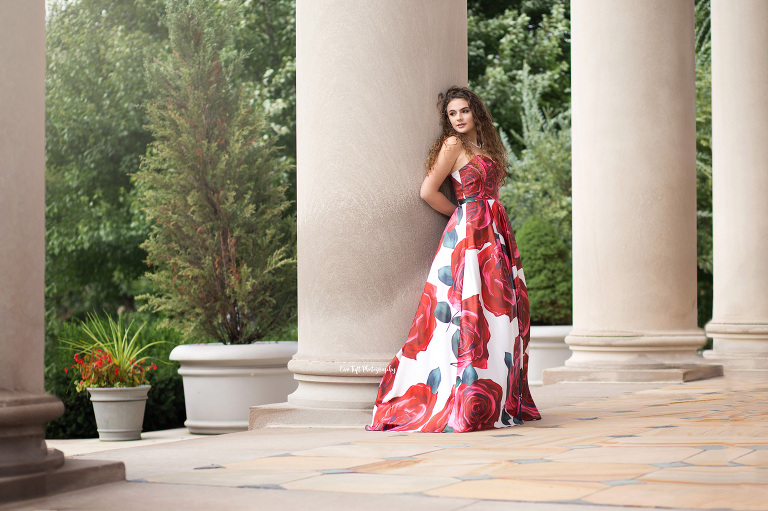 Teenager in a formal floral dress leaning up against some church pillars outside. | Saginaw Senior portraits