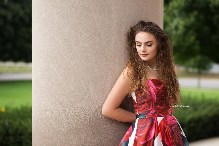 Teenager in a formal floral dress leaning up against some church pillars outside. | Saginaw Senior portraits