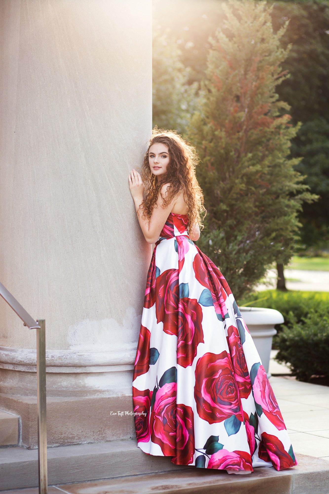 Teenager in a formal floral dress leaning up against some church pillars outside. | Saginaw Senior portraits