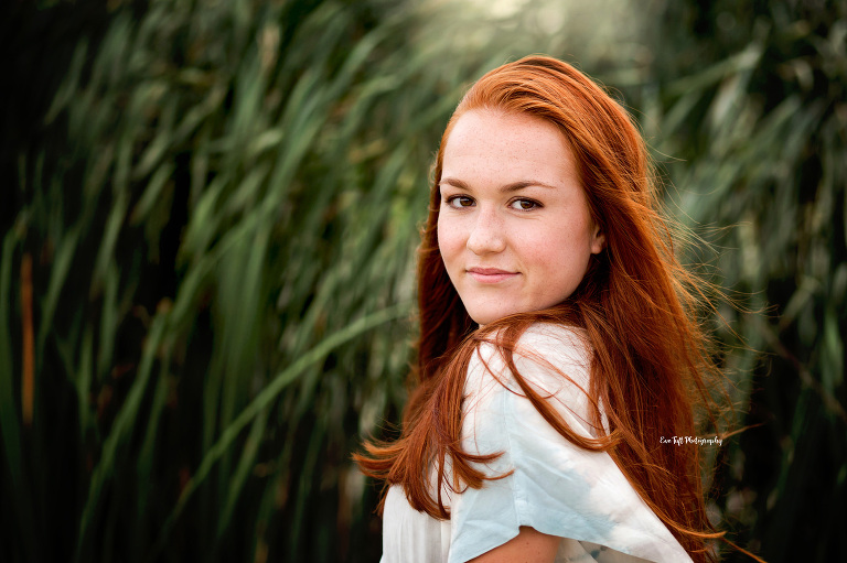 Head shot of a red-head high school girl with some tall, green reeds at the beach. Michigan senior Photographer