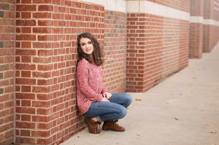 Senior girl squatting and leaning against a brick wall in downtown Midland, Michigan