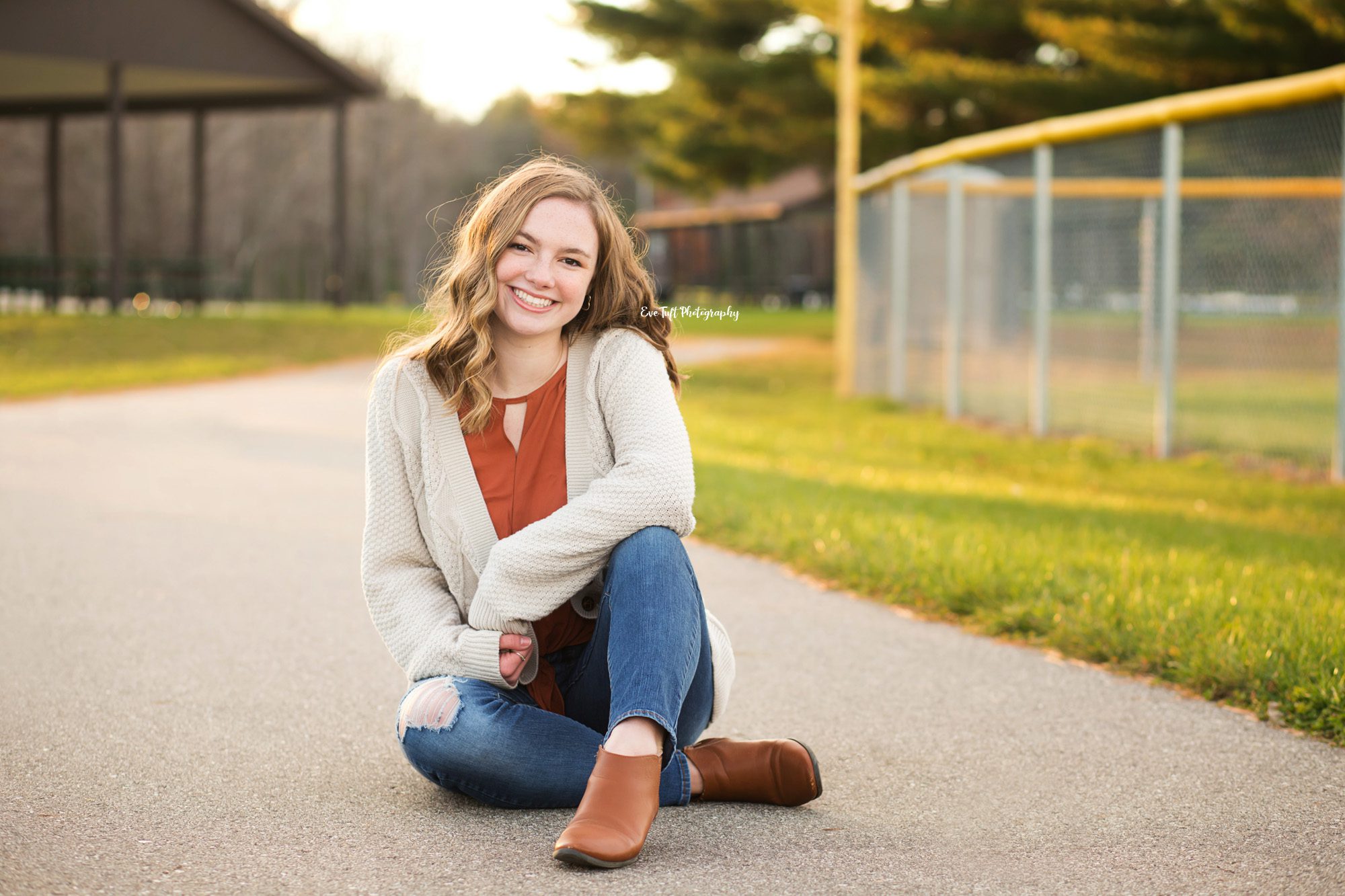 Senior girl sitting down on a pathway at a park smiling at the camera | Eve Tuft Photography, senior portraits