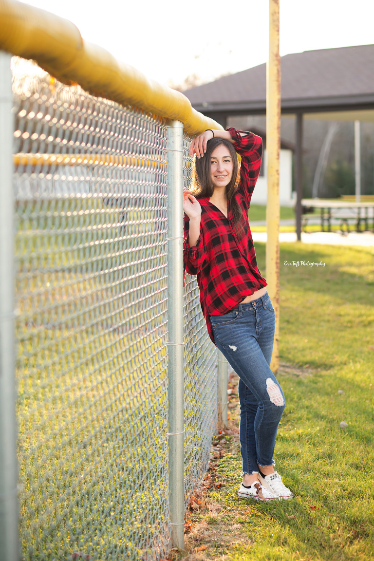 Teenage girl leaning up against a chain link fence | Senior Portraits by Eve Tuft Photography