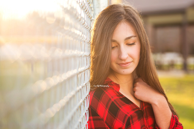 Teenage girl leaning against a fence and looking down for her senior portraits | Eve Tuft in Midland, Michigan