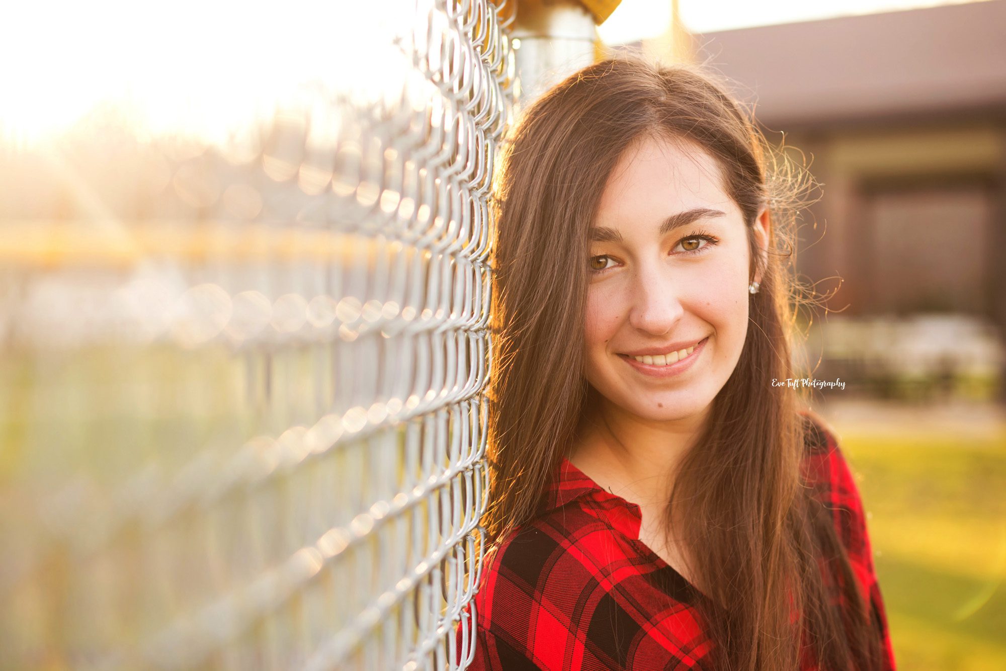 Brown haired senior girl leaning up against a chain-link fence and smiling at the camera | Eve Tuft | Michigan Photographer