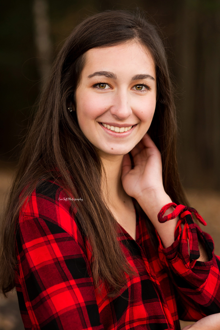 Senior girl wearing flannel smiling at the camera with one hand by her neck | Michigan High School Photographer