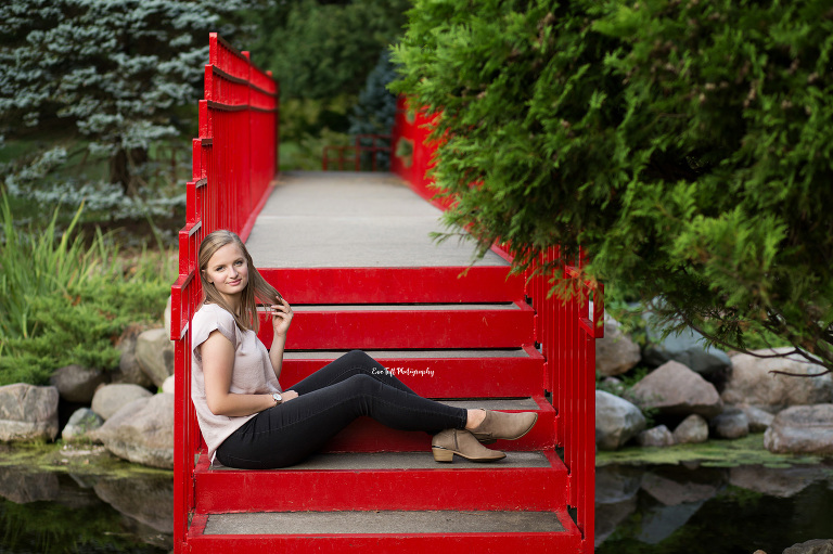 Senior girl sitting down on a red bridge at Dow Gardens outside | Michigan Photographer