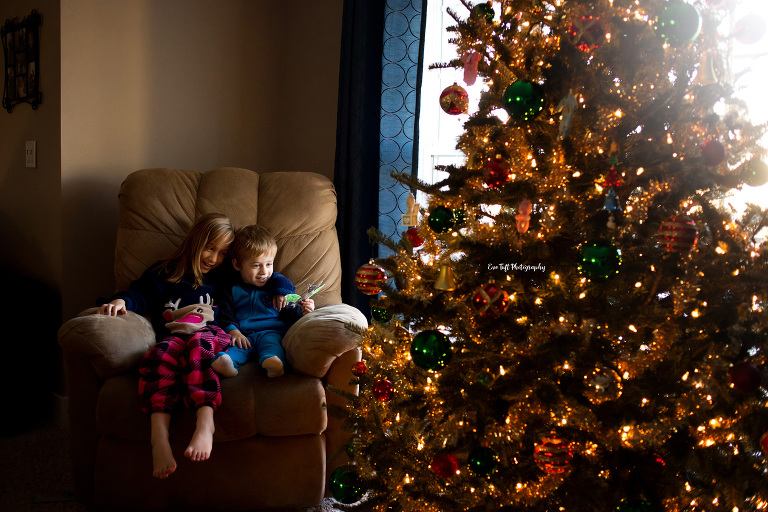 Two children sit on a rocking chair together at Christmastime next to a Christmas tree | Bay City Senior Photographer