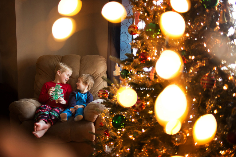 Two brothers sitting on a chair giggle while looking at each other next to a Christmas tree | High School Senior Photographer in Michigan