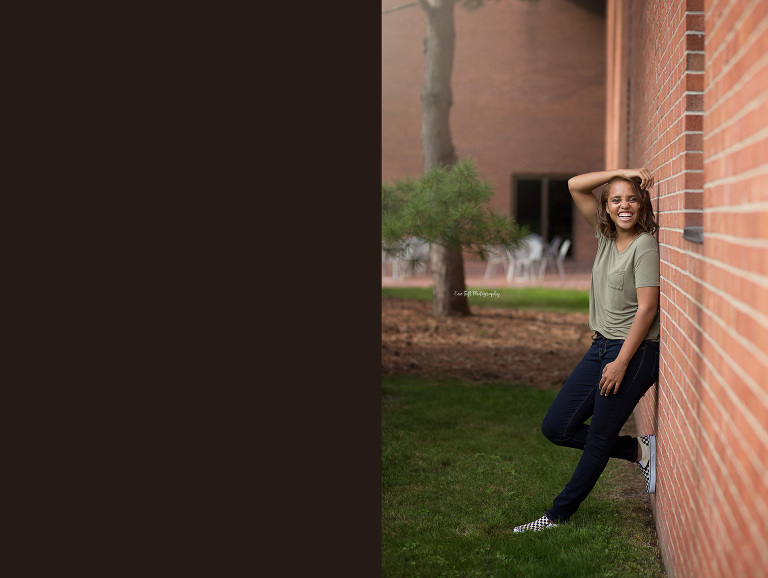 High School Senior girl standing against a brick wall while laughing | Michigan Photographer