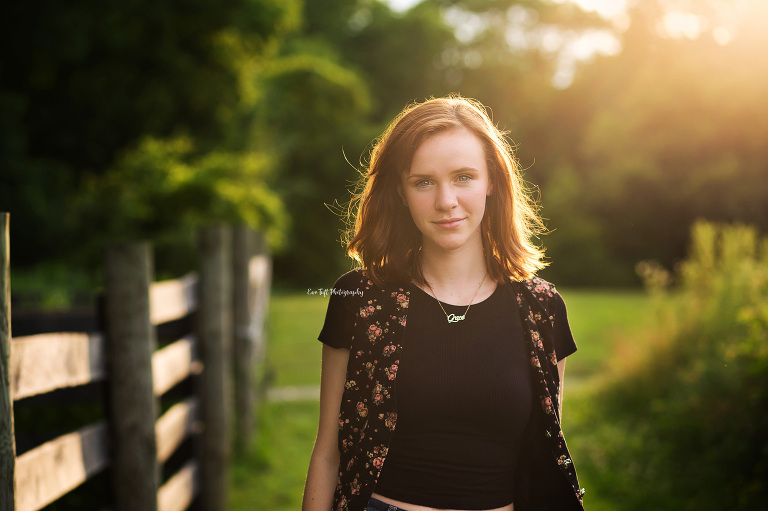 Senior girl standing next to a brown fence in the sunlight for her high school photos | Saginaw Teen Photographer