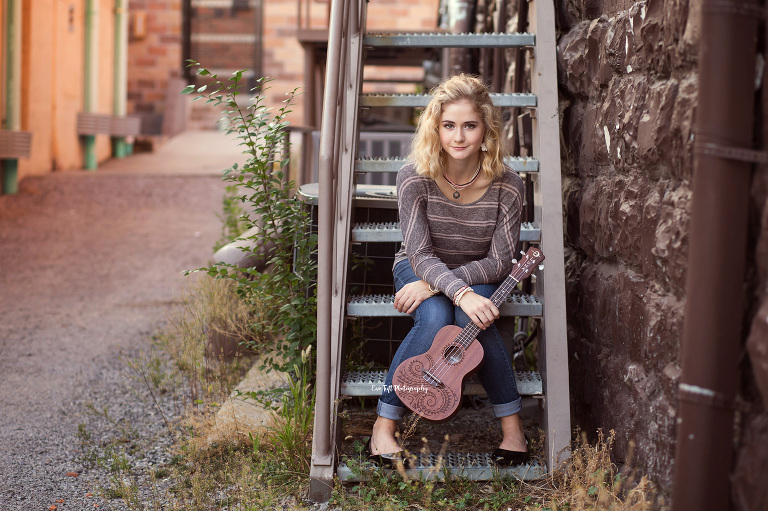 A senior girl sitting on some stairs holding her ukulele in an alley in Midland | Michigan senior photographer