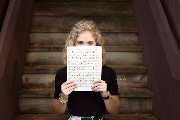 Senior girl holding up sheet music while sitting on stairs at Dow Gardens | High School Photographer Eve Tuft