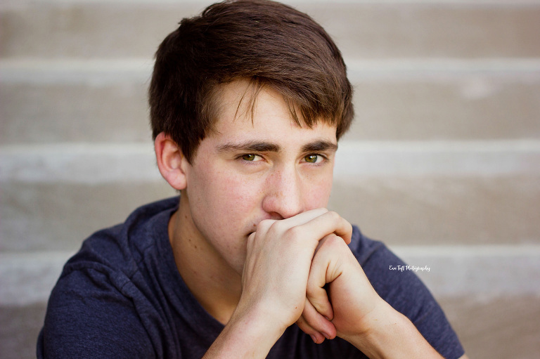 Senior boy looking at the camera with his hands together by his chin | Michigan Photographer