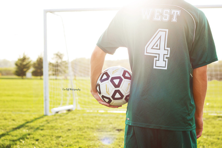 Soccer player holding the ball under his arm while facing the net | Senior Portrait Photographer