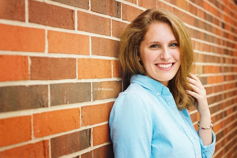 High School senior girl leaning against a brick wall and touching her hair | Saginaw Senior Photographer