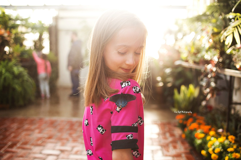 Girl in a pink shirt in a greenhouse with a butterfly on her shirt | Eve Tuft, a senior photographer in Michigan