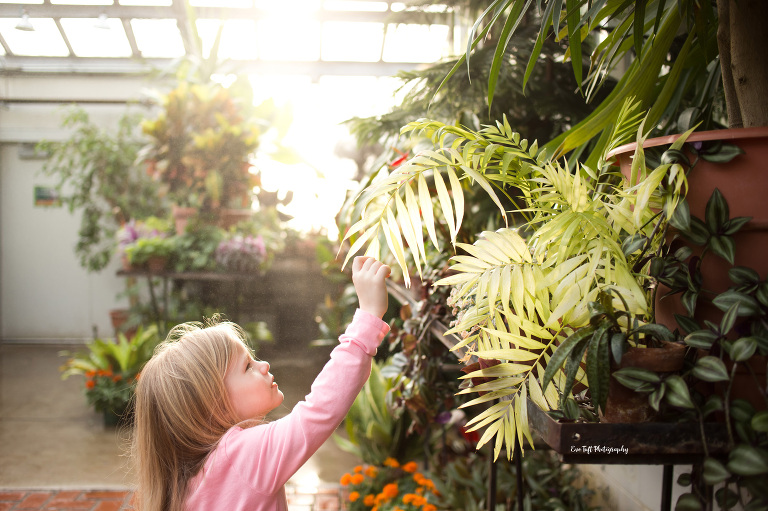 Little girl in a pink shirt in a greenhouse with some plants in Midland, Michigan | Senior Portrait Photographer Eve Tuft