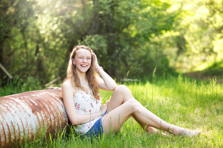 Senior girl sitting against a pipe outside on the ground, laughing | Senior Photographer in Michigan