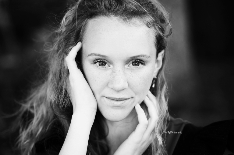 Close up in black and white of a teenage girl looking up at the camera with her hands on her face