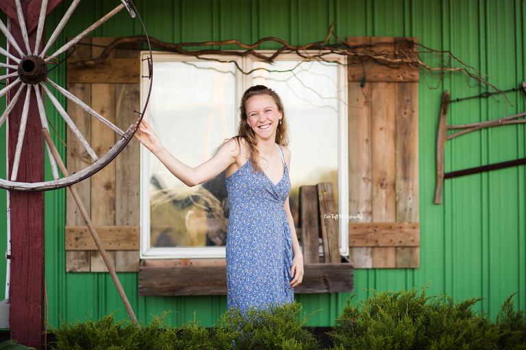 Senior girl standing in front of a window holding onto a wheel while smiling | Michigan Senior Photographer