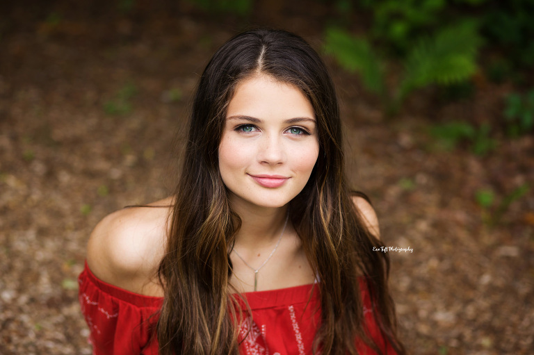 Senior girl sitting on the ground outside and smiling up at the camera | Senior Photographer in Midland, Michigan