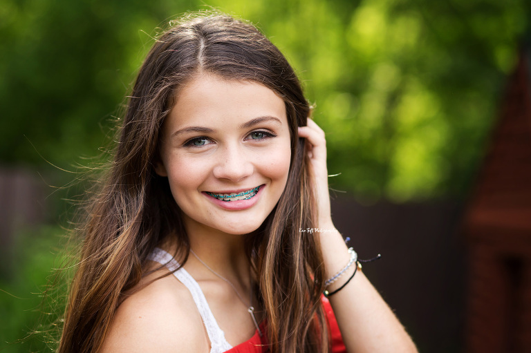 Close up of a high school girl smiling at the camera and tucking her hair behind her ear | Senior Photographer in Michigan