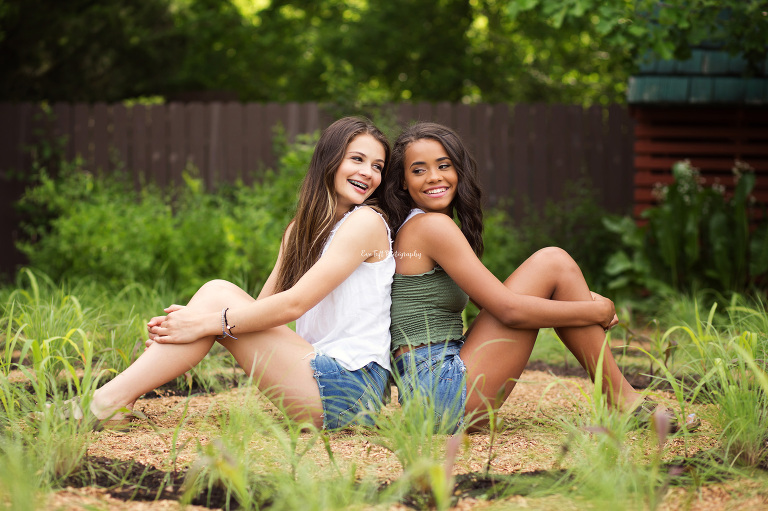 Two girls sitting back to back outside at Dow Gardens in Midland, Michigan | Portrait Photographer