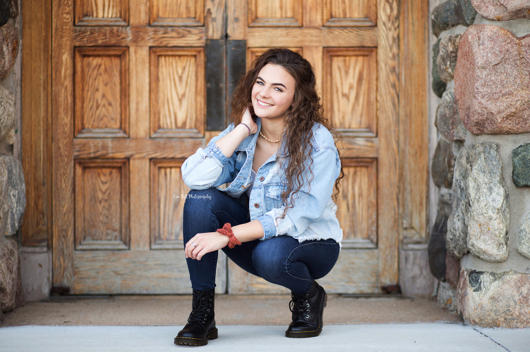 Senior girl squatting in front of the courthouse doors in Midland, MI | Senior Photographer