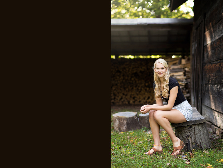 A senior girl sitting on a wooden log outside of a barn | Senior Photographer in Midland, MI