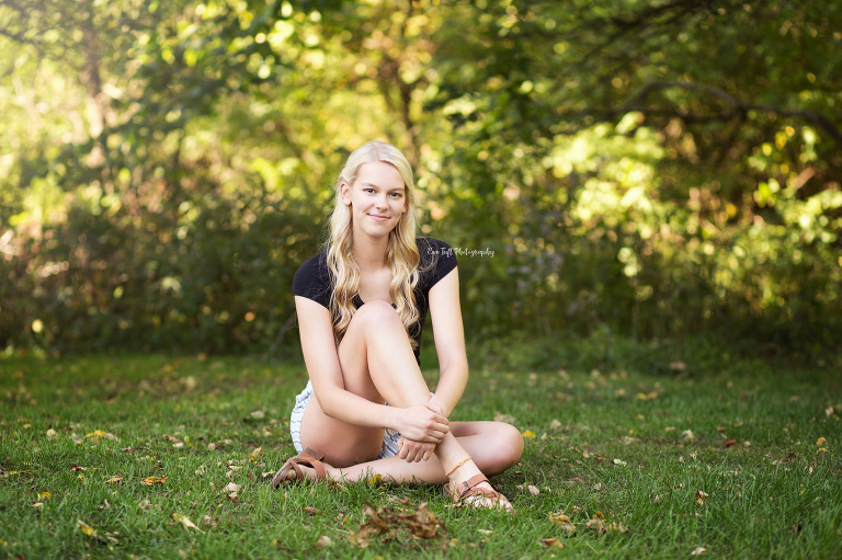 High School senior girl sitting in the grass and holding onto her leg | Senior Photography in Midland, Michigan
