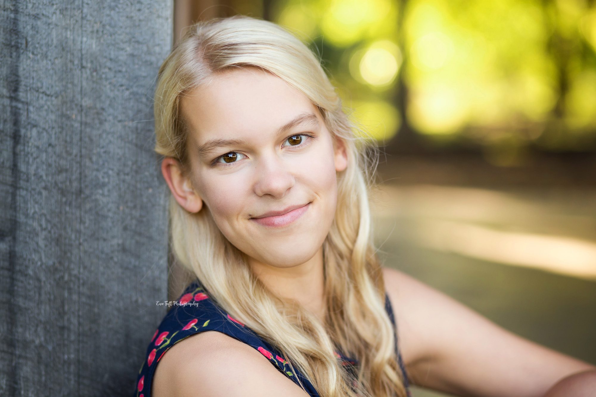 Teenage girl softly smiling while leaning her head against an old barn door | Reschedule photo shoot with Grace