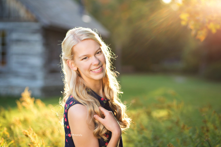 Gorgeous senior girl outside in front of a barn during golden hour holding onto her hair | Senior photographer in Midland, Michigan