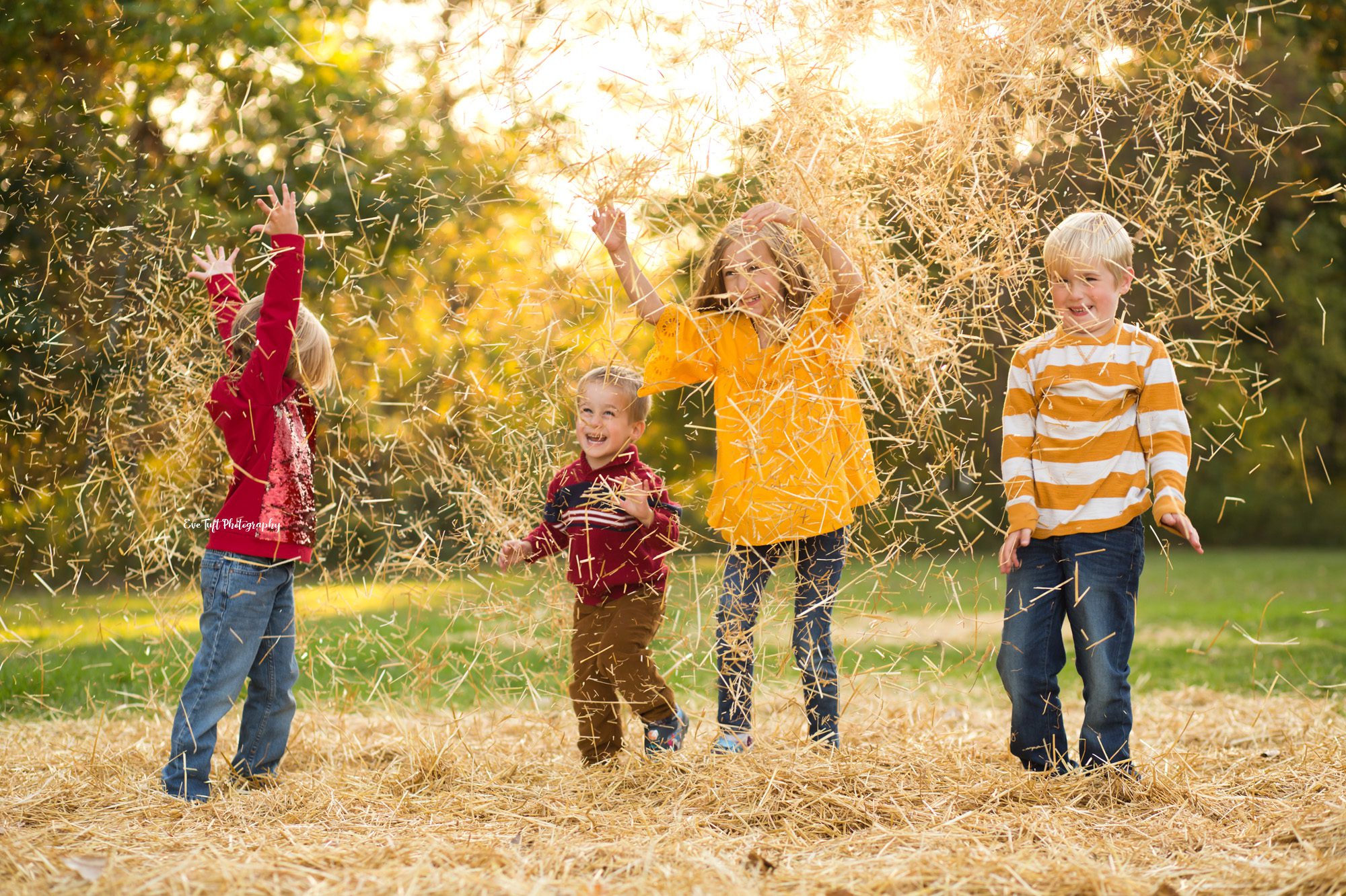 Four kids throw hay up into the air outside for fun | Senior Photographer