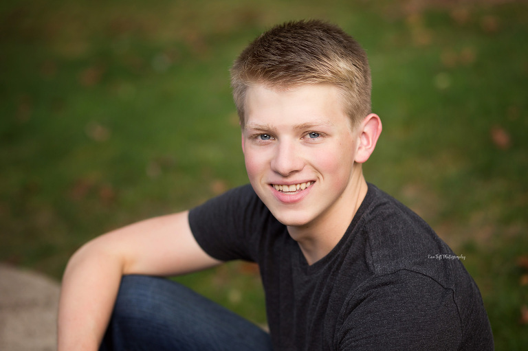 A Senior guy smiles at the camera outside for a head shot for his senior pictures | Photographer in Michigan