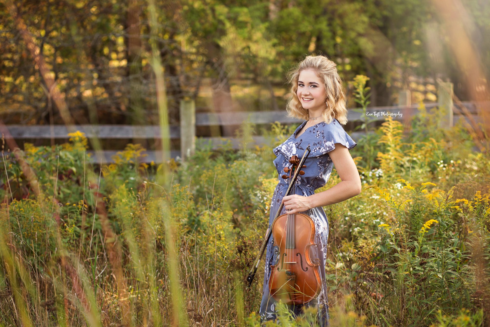 A teenage girl holds her viola as a prop in a field of flowers for her photo shoot | Senior Photographer in Midland, MI