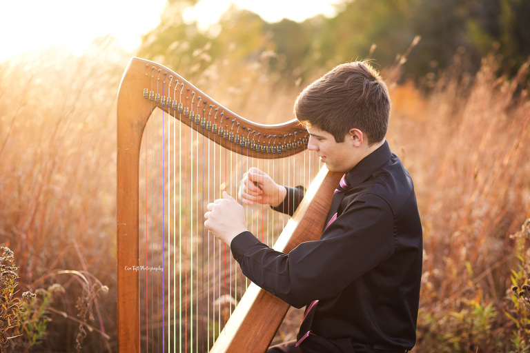 A senior guy plays his harp out in a golden field in Midland, Michigan | Photographer