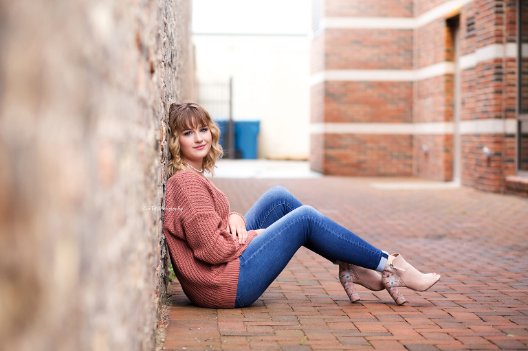 A senior girl sits down in an alley way in downtown Midland, Michigan | Senior Photographers in Michigan