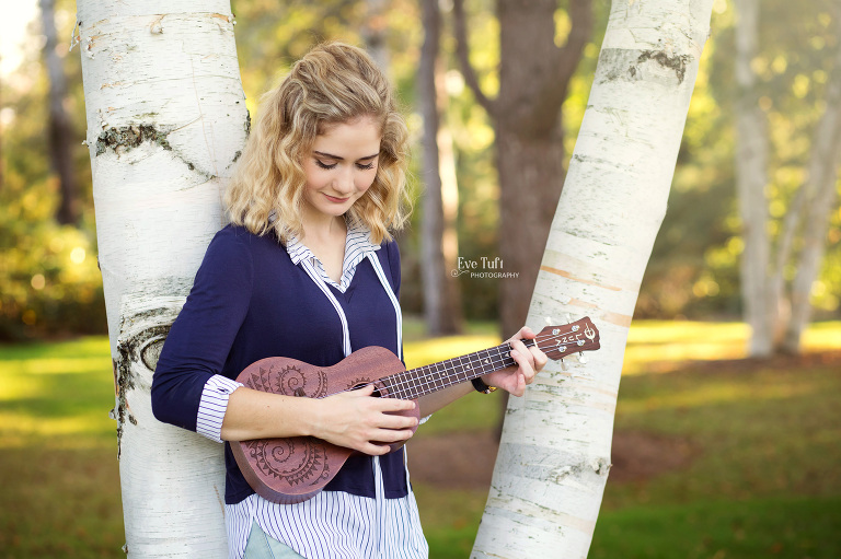 A teenage girl leans against a tree while playing her ukulele | Midland, Michigan senior photographers