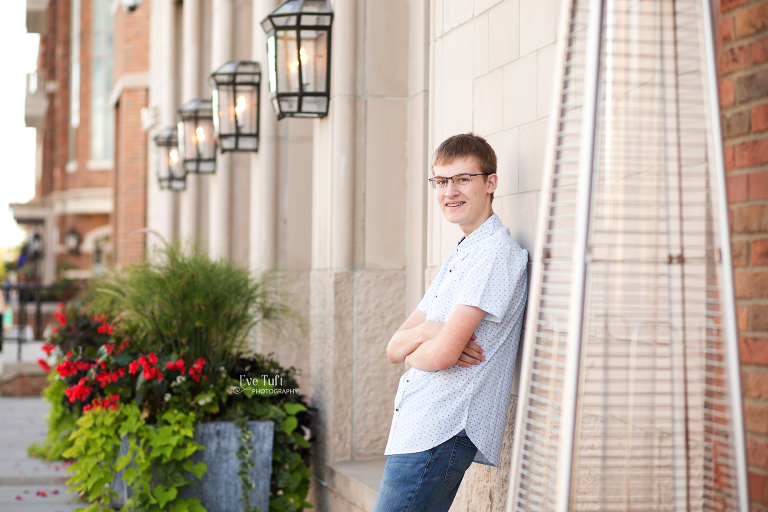 A teenage boy leans up against a building while crossing his arms in downtown Midland, Michigan | Senior photographer near me