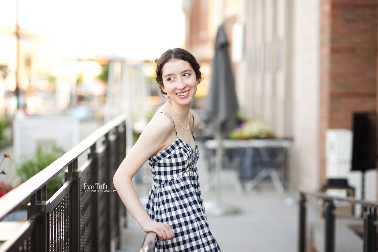 A teenage girl leans against a black railing while smiling over her shoulder | Senior photographers in Midland, Michigan