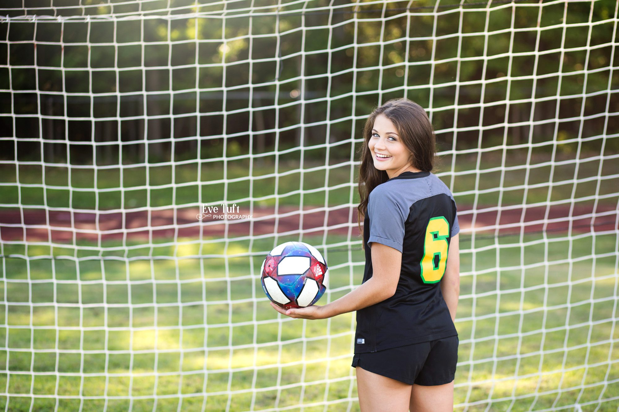 A senior girl holds a soccer ball while looking over her shoulder for her sports photos | Senior Photographers in Midland, MI