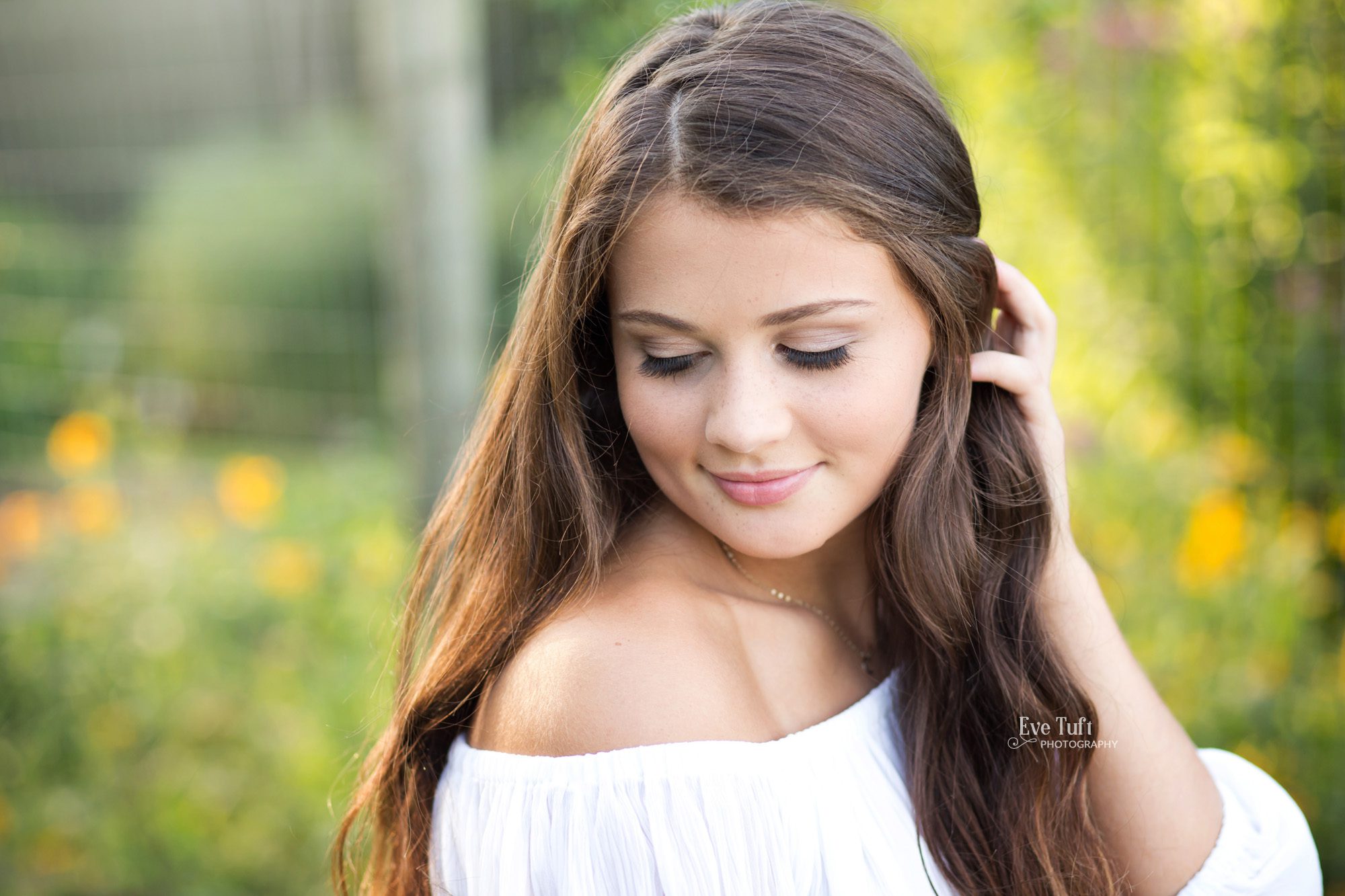 A senior girl looks down at the ground while brushing her hair back from her face for her senior portraits | Senior Photographer in Midland, Michigan