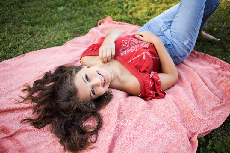 A senior girl lies down on a blanket and smiles at the camera | Senior Photographer in Midland, MI