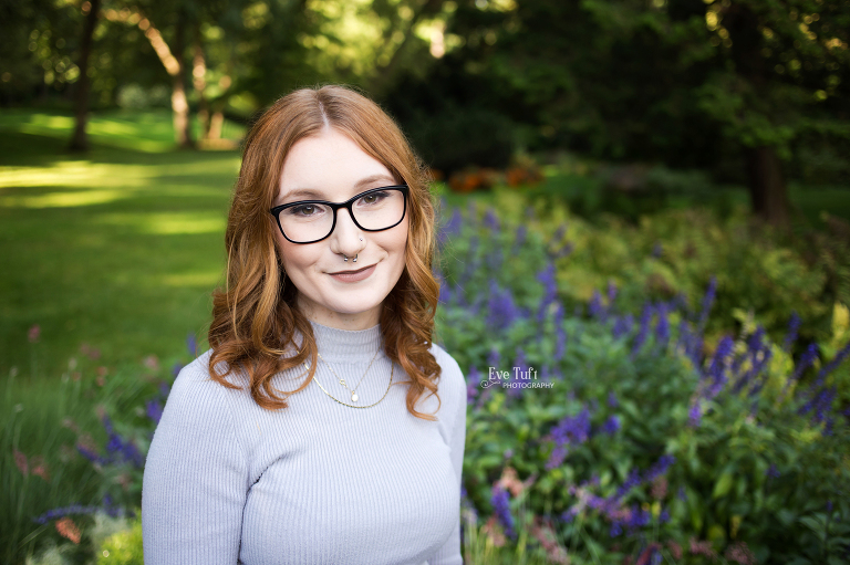 A senior girl with glasses poses in front of purple flowers in Midland, Michigan | Dow Gardens Senior Photographer