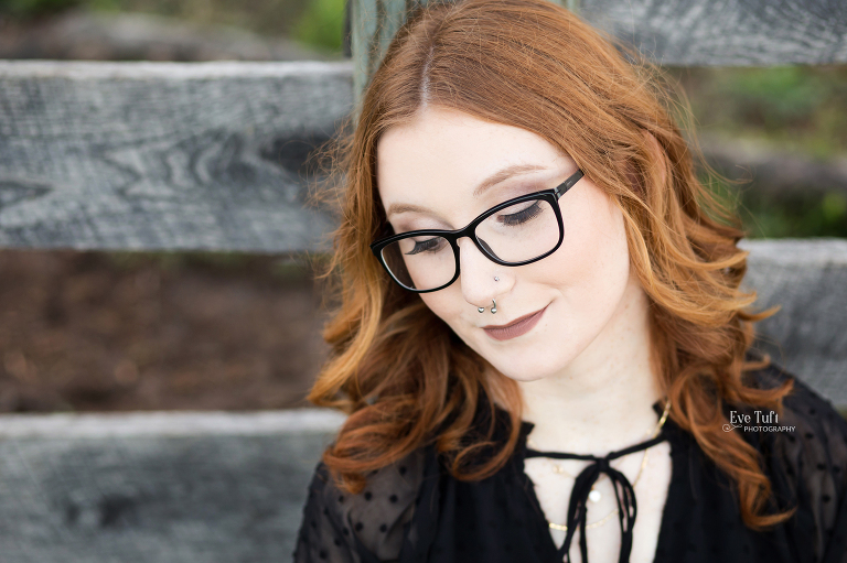 A senior girl looks off to the side in front of a fence in Midland, MI